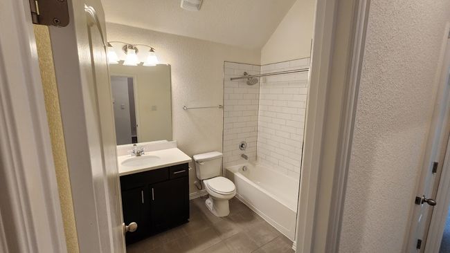 Bathroom featuring a textured wall, vaulted ceiling, toilet, vanity, and bathtub / shower combination | Image 12