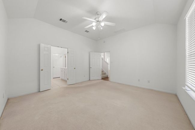 Unfurnished bedroom featuring a ceiling fan, visible vents, vaulted ceiling, ensuite bathroom, and light colored carpet | Image 11