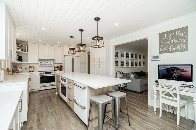 Kitchen with wood finished floors, white appliances, a breakfast bar area, open shelves, and a kitchen island | Image 6