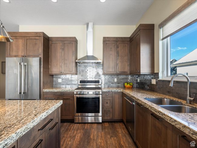 Kitchen with stainless steel appliances, wall chimney range hood, a sink, dark wood-style floors, and light stone counters | Image 15