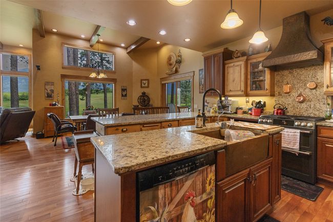Kitchen with custom exhaust hood, range with two ovens, dishwashing machine, an island with sink, and wood-type flooring | Image 13