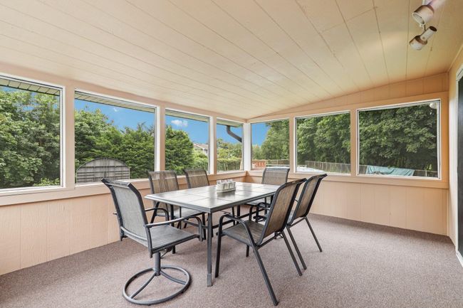 Sunroom featuring carpet floors, track lighting, outdoor dining space, a chandelier, and wood walls | Image 19