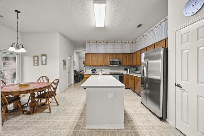 Kitchen with stainless steel appliances, brown cabinets, a textured ceiling, light countertops, and an island with sink | Image 17