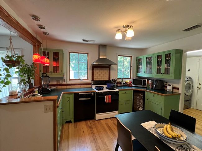 Kitchen featuring stainless steel microwave, range with gas stovetop, wall chimney range hood, black dishwasher, and green cabinetry | Image 5