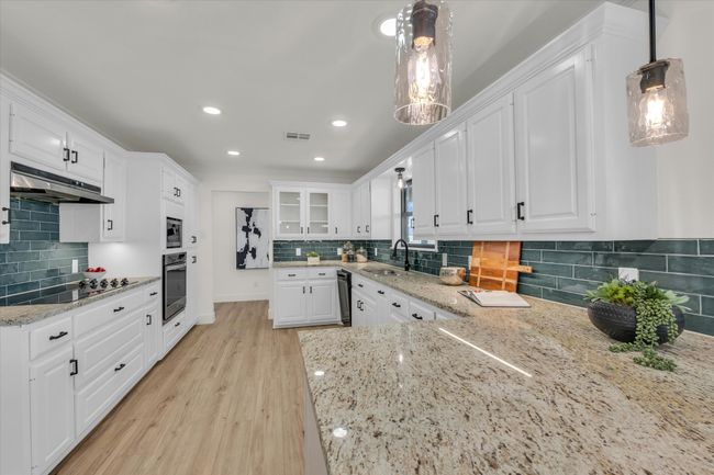 Kitchen featuring visible vents, white cabinets, a sink, under cabinet range hood, and black appliances | Image 18
