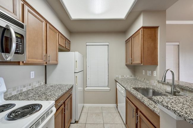 Kitchen with white appliances, brown cabinets, light stone countertops, and light tile patterned flooring | Image 14