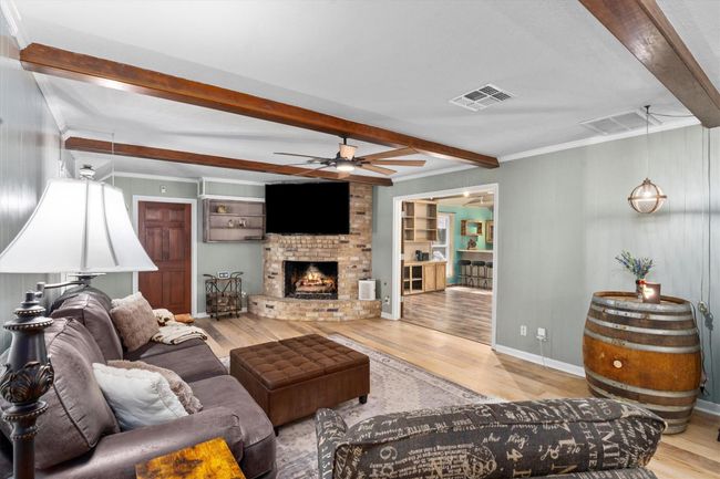 This inviting living room features exposed wooden beams, a cozy brick fireplace, and a spot to have your TV mounted. The space is open to the kitchen area, offering a seamless flow for entertainment. | Image 15