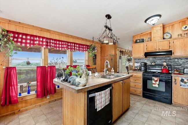 Kitchen with black appliances, under cabinet range hood, healthy amount of natural light, decorative backsplash, and wood walls | Image 13