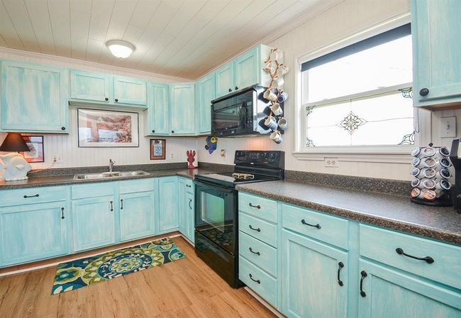 This bright kitchen features charming turquoise cabinets, a sleek black oven, and a large window with decorative glass. The space is accented by gorgeous flooring and modern countertops, offering a stylish cooking area. | Image 11