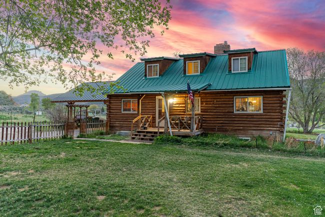 Back of house at dusk with log exterior, a chimney, metal roof, and covered porch | Image 4