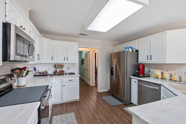 Kitchen featuring dark wood finished floors, stainless steel appliances, light countertops, tasteful backsplash, and white cabinetry | Image 7