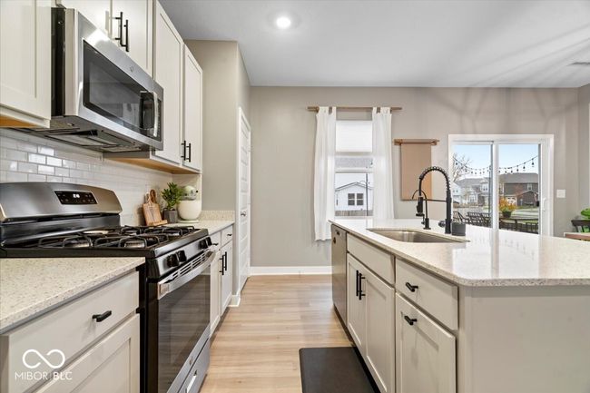 kitchen featuring stainless steel appliances, light wood-type flooring, tasteful backsplash, an island with sink, and white cabinetry | Image 15