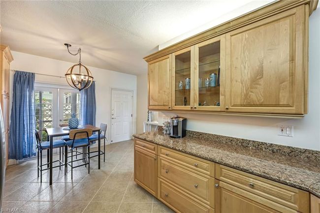 Kitchen with a chandelier, dark stone countertops, glass insert cabinets, hanging light fixtures, and a textured ceiling | Image 7