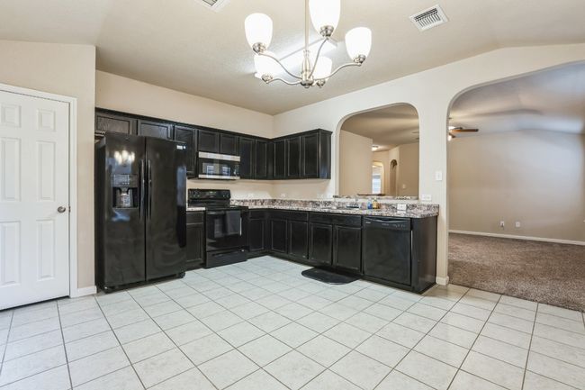 Kitchen with pendant lighting, light stone counters, black appliances, and light tile patterned flooring | Image 7