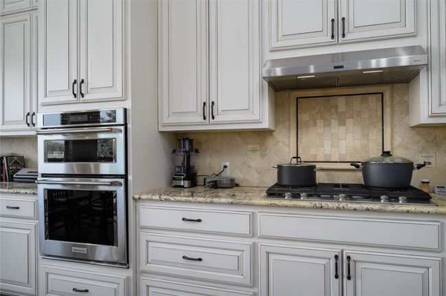 Kitchen with ornate backsplash, appliances with stainless steel finishes, under cabinet range hood, and white cabinets | Image 14