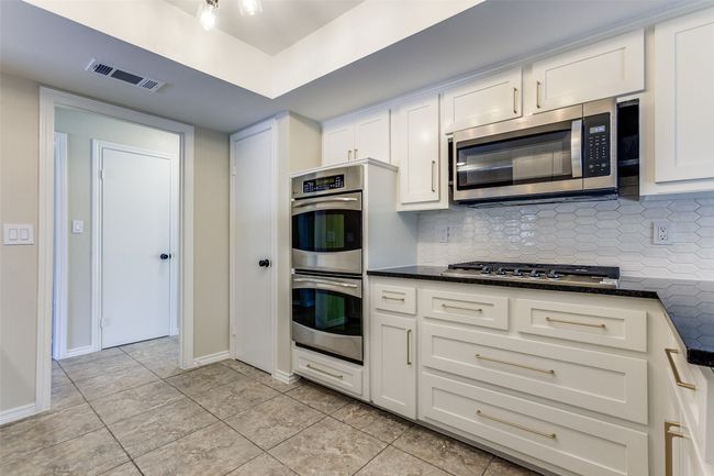 Kitchen featuring appliances with stainless steel finishes, backsplash, white cabinetry, light tile patterned floors, and dark stone counters | Image 14