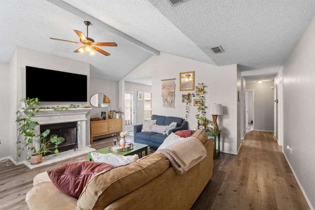 Living room featuring wood finished floors, a ceiling fan, a fireplace with raised hearth, a textured ceiling, and baseboards | Image 5