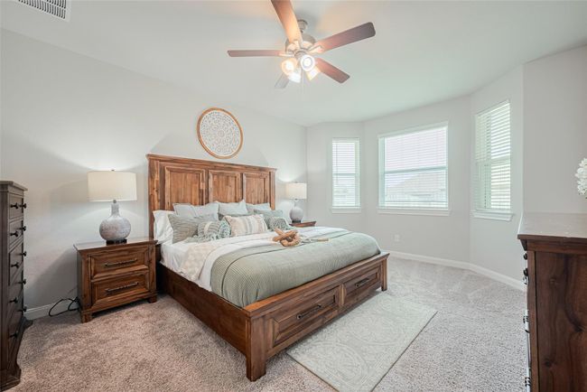 This bedroom features a spacious layout with large windows for ample natural light and a ceiling fan for comfort. Neutral walls and carpeting create a warm, inviting atmosphere. | Image 24