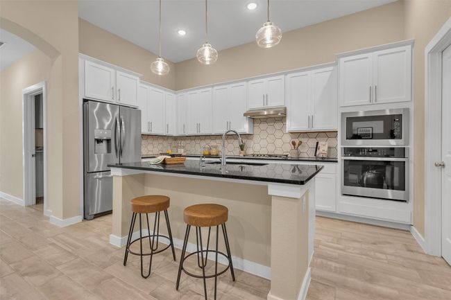 Kitchen with arched walkways, stainless steel appliances, decorative backsplash, white cabinets, and a breakfast bar area | Image 10
