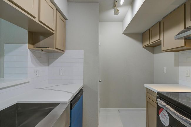 This photo showcases a modern kitchen with light cabinetry, white countertops, and a sleek backsplash. It features stainless steel appliances, including a dishwasher and an electric stove, and is well-lit with track lighting. | Image 9