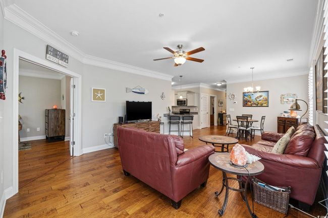 Living area with ceiling fan, wood finished floors, ornamental molding, a chandelier, and baseboards | Image 12