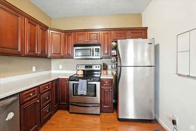 Kitchen featuring stainless steel appliances, light countertops, light wood finished floors, and a textured ceiling | Image 10