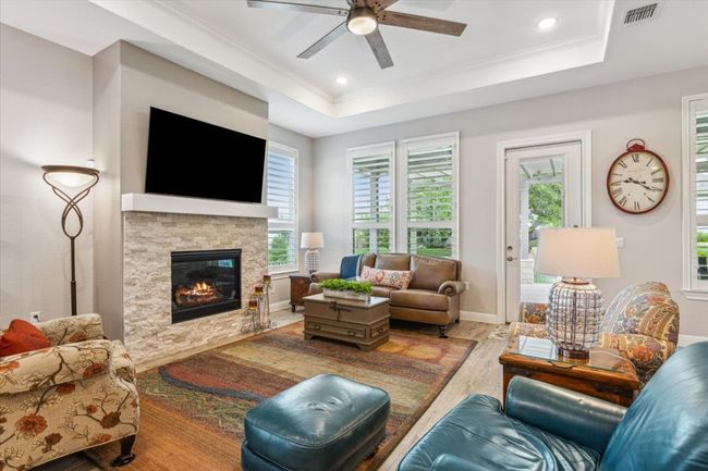Great room with wood look tiled floors, an upgraded ceiling fan, healthy amount of natural light & a framed dropped soffit with crown molding | Image 8