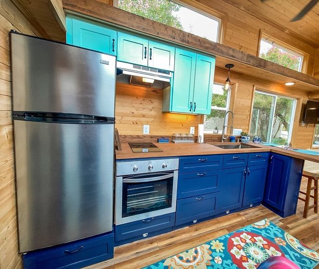 Kitchen with appliances with stainless steel finishes, blue cabinets, under cabinet range hood, wood walls, and light wood-style floors | Image 23