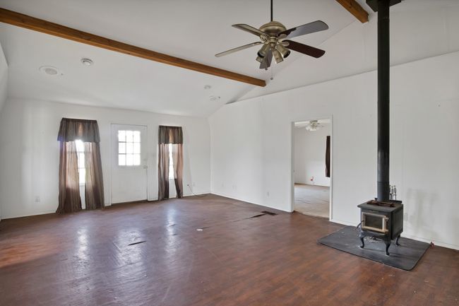 Unfurnished living room featuring a wood stove, beamed ceiling, a ceiling fan, wood finished floors, and high vaulted ceiling | Image 6