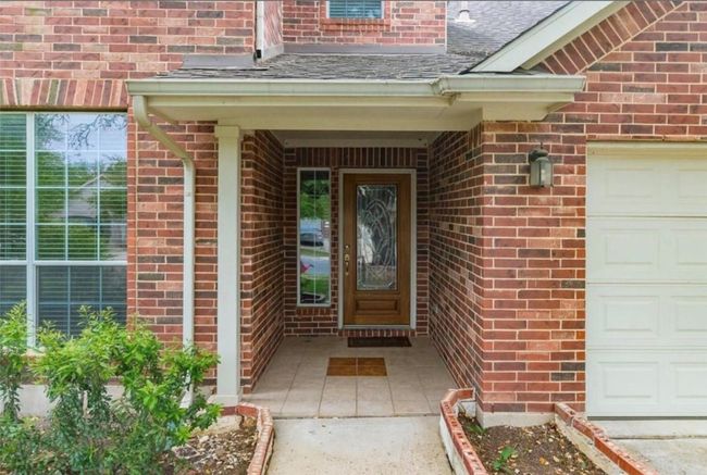 Doorway to property with brick siding, an attached garage, and a shingled roof | Image 4