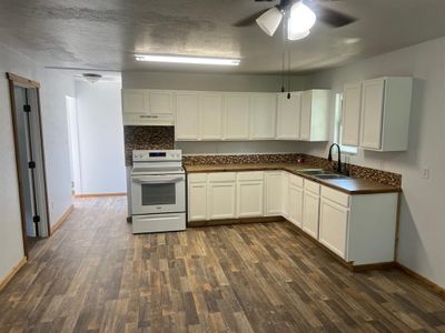 Kitchen with dark hardwood / wood-style floors, ceiling fan, white cabinetry, electric range, and sink | Image 3