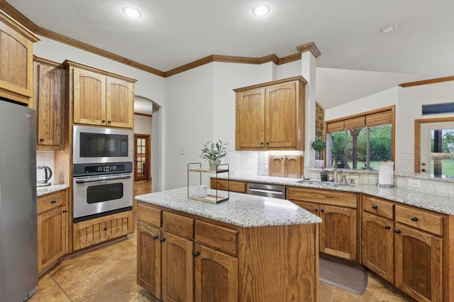 Kitchen with stainless steel appliances, arched walkways, decorative backsplash, ornamental molding, and a kitchen island | Image 13