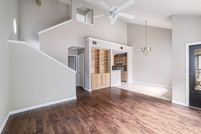 Unfurnished living room featuring high vaulted ceiling, a chandelier, ceiling fan, wood finished floors, and baseboards | Image 4