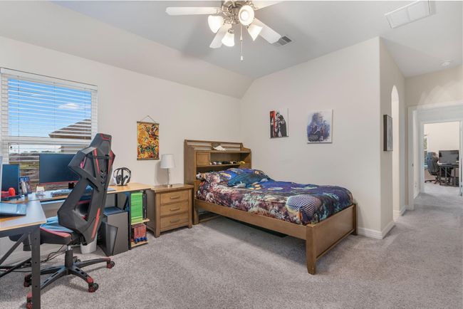 This spacious bedroom features plush carpeting, a ceiling fan, and ample natural light from a large window. It includes a functional workspace ideal for comfort and productivity. | Image 37