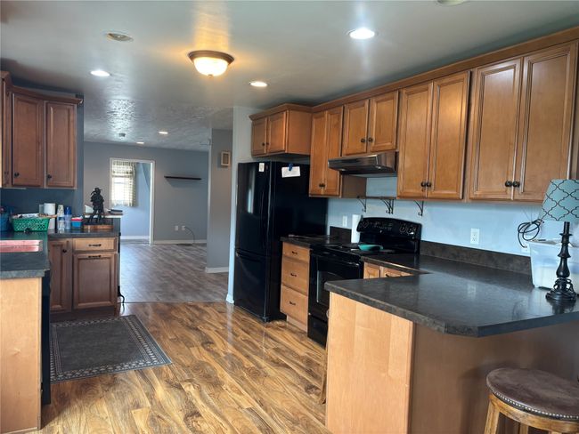 Kitchen with black appliances, under cabinet range hood, a peninsula, dark countertops, and wood finished floors | Image 10
