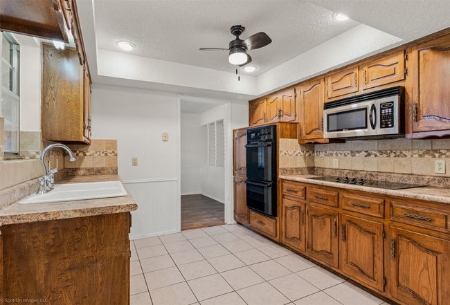 Kitchen with black appliances, a sink, a textured ceiling, a ceiling fan, and light tile patterned floors | Image 11