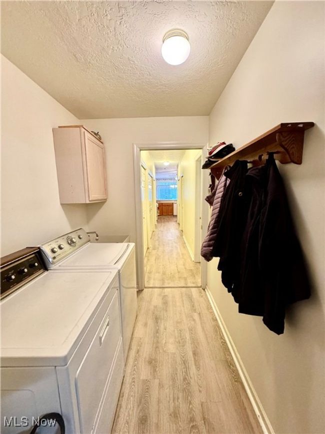 Clothes washing area with cabinets, a textured ceiling, washer and clothes dryer, and light hardwood / wood-style flooring | Image 25