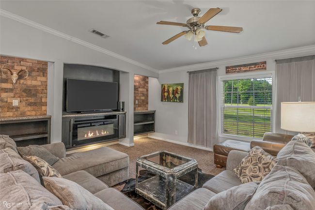Living room featuring carpet flooring, ceiling fan, a glass covered fireplace, crown molding, and baseboards | Image 8