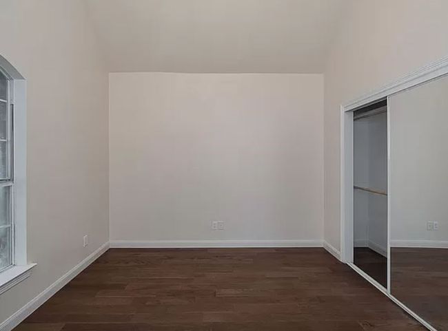 Unfurnished bedroom with wood finished floors, a closet, and arched walkways | Image 12