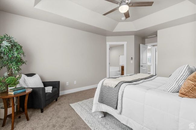Bedroom with a raised ceiling, light colored carpet, baseboards, connected bathroom, and a ceiling fan | Image 20