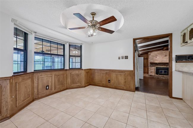 Empty room featuring light tile patterned floors, a wainscoted wall, a brick fireplace, and a textured ceiling | Image 14