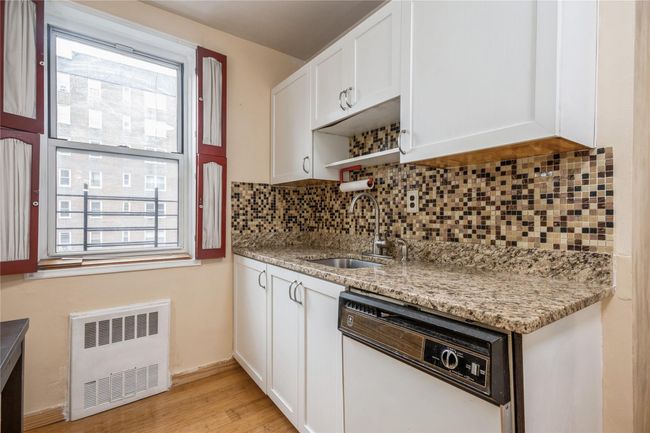 Kitchen featuring radiator heating unit, white dishwasher, decorative backsplash, white cabinetry, and healthy amount of natural light | Image 7