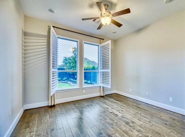 Bright room with large windows, wooden floors, and a ceiling fan. The space opens to a view of a fenced backyard with greenery. | Image 14