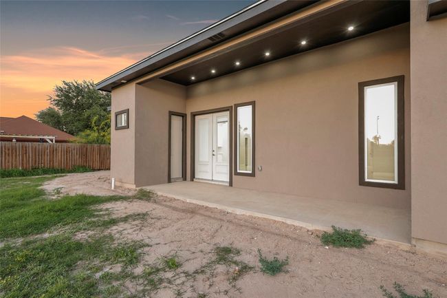 This photo showcases a modern home exterior with a simple concrete patio, recessed lighting, and a fenced backyard. The space offers potential for landscaping and outdoor activities. | Image 9