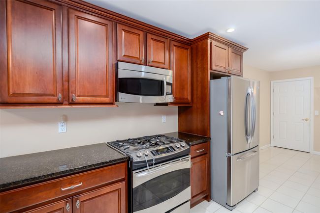 Kitchen with appliances with stainless steel finishes, light tile patterned floors, dark stone countertops, brown cabinetry, and recessed lighting | Image 11