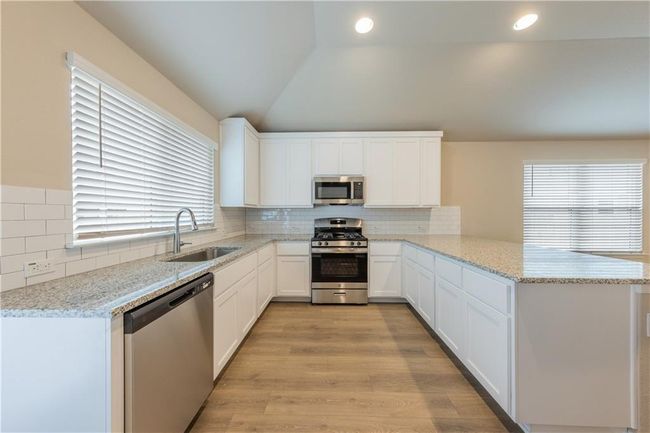 Kitchen featuring appliances with stainless steel finishes, a sink, a peninsula, vaulted ceiling, and plenty of natural light | Image 7