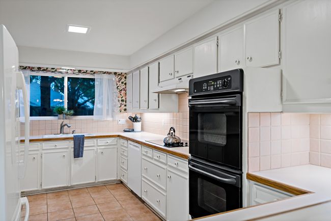 Kitchen with white cabinets, white appliances, light tile floors, backsplash, and under cabinet range hood | Image 12