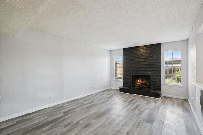 Unfurnished living room featuring wood finished floors, a fireplace, and a textured ceiling | Image 5