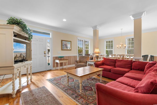 Living room featuring light wood-type flooring, crown molding, a wainscoted wall, a chandelier, and ornate columns | Image 11