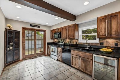 Kitchen featuring beam ceiling, sink, beverage cooler, black appliances, and decorative backsplash | Image 3